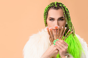 Transgender makeup artist with brushes on color background