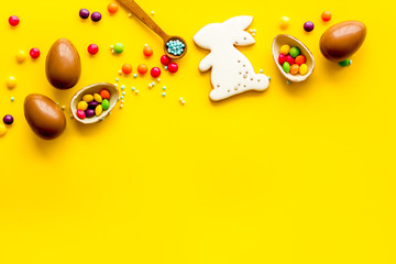 Easter sweets frame. Chocolate eggs and bunny gingerbread on yellow background top-down frame copy space