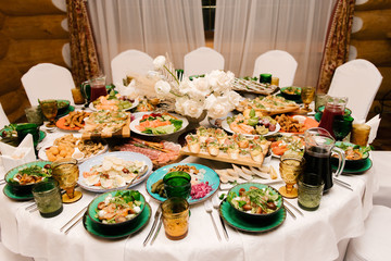The round white table is filled with a large amount of food and various snacks in a luxurious interior, beautiful serving of the holiday table