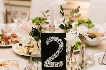 Round white table with snacks in a luxurious interior, table setting,table number card and flowers, selective focus