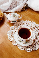 Horizontal photo of Breakfast with a white porcelain Cup on a knitted white napkin and a painted teapot in the background, ready-made pancakes on a saucer. Table setting for the holiday Maslenitsa.