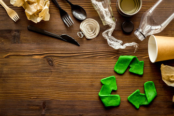 Green recycle icon near plastic, paper, glass waste on dark wooden background top-down copy space
