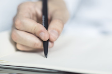 Man writes with a pen in notebook in a sunny office, business and education concept. Close up