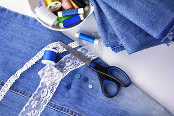 Jeans fabric for sewing, lace and accessories for needlework on whiten background. Spool of thread, scissors, buttons, sewing supplies. Set for needlework