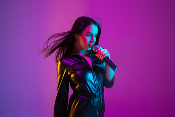 Caucasian female singer portrait isolated on purple studio background in neon light. Beautiful...