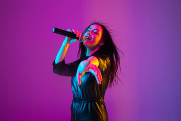Caucasian female singer portrait isolated on purple studio background in neon light. Beautiful...