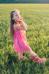 Portrait of a girl in a pink dress on green grass in a field