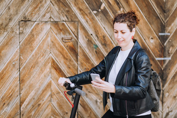 Middle aged woman riding his electric scooter and looking at mobile phone.