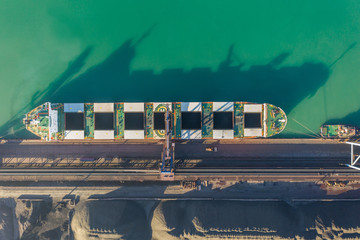 A bulk carrier stands at the berth of a coal terminal in the seaport, cargo is being loaded from an open warehouse onto a ship with a conveyor belt and a ship loading machine.