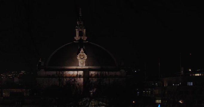Slow motion wide shot with parallax camera movement of dark tree branches in front of the famous and illuminated National Theatre building in Karl Johan main parade street at night, Oslo Norway.