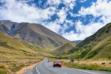 A red car ran on a highway in the valley at the Lindis Pass Summit scenic look out in summer season in Otago, New Zealand. © Lowpower
