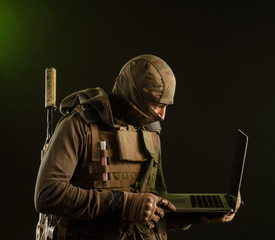saboteur soldier in military clothing with a weapon on a dark background with a laptop