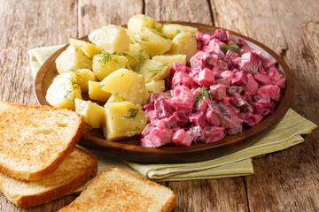 Winter German herring salad with vegetables and a side dish of boiled potatoes close-up in a plate. horizontal