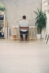 Back view of an young male architect sitting at his desk and typing.