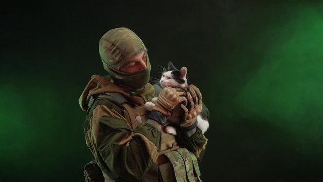 a saboteur soldier in military clothing with a weapon on a dark background holds a kitten in his hands