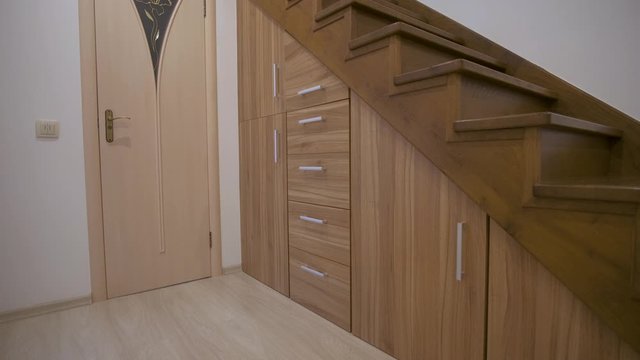 Modern architecture interior with luxury hallway with glossy wooden stairs in multi-storey house. Custom built pullout cabinets on glides in slots under stairs. Use of space for storage.