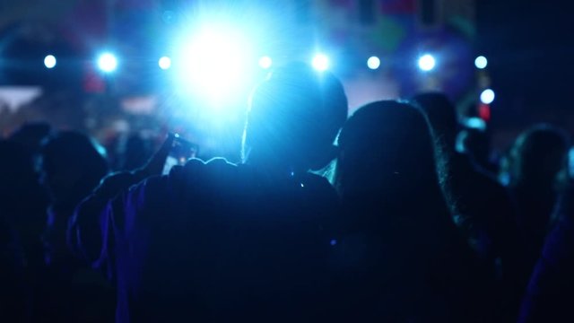 People enjoying night music festival, dancing and taking photos of atmosphere with beautiful lights
