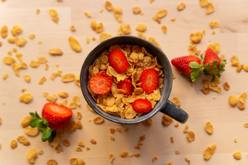 healthy corn flakes breakfast bowl on wooden table with corn flakes, strawberries and fruit with natural light