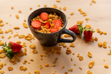healthy corn flakes breakfast bowl on wooden table with corn flakes, strawberries and fruit with natural light
