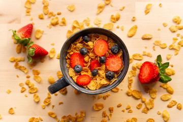 healthy corn flakes breakfast bowl on wooden table with corn flakes, strawberries and blueberries and fruit with natural light