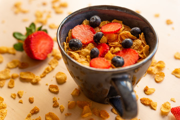 healthy corn flakes breakfast bowl on wooden table with corn flakes, strawberries and blueberries and fruit with natural light