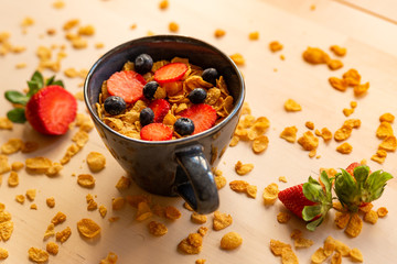 healthy corn flakes breakfast bowl on wooden table with corn flakes, strawberries and blueberries and fruit with natural light