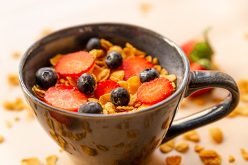 close up of healthy corn flakes breakfast bowl on wooden table with corn flakes, strawberries and blueberries and fruit with natural light