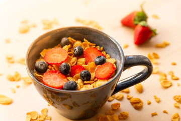 healthy corn flakes breakfast bowl on wooden table with corn flakes, strawberries and blueberries and fruit with natural light