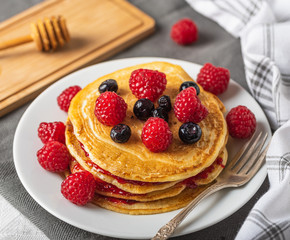 Sweet homemade pancakes with raspberries and blueberries on white plate.