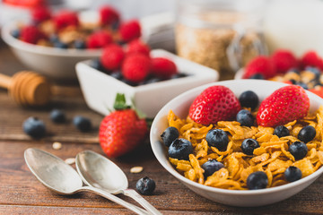 Granola chips with blueberries and raspberries in white bowl in dark wooden desk.