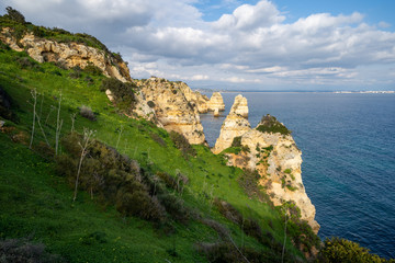 Fototapeta na wymiar Steep, sloped natural cliff formations of Algarve coastline with green grass at Ponta da Piedade, in Algarve Portugal