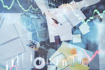 Hand taking notes in notepad. Forex chart holograms in front. Concept of research. Double exposure