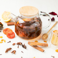 glass teapot with black tea on a white table with a composition of spices and dried fruits