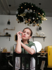 Young girl in a white T-shirt and a green cardigan draped over her shoulders sits on a wooden chair in a stylish kitchen