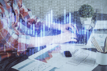 Double exposure of stock graph with businessman typing on computer in office on background. Concept of hard work.