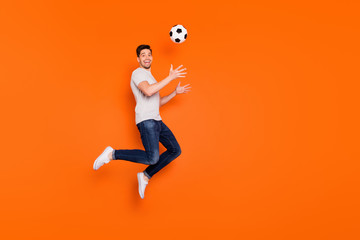 Full body profile photo of funny guy jump high up catch football ball addicted fan goalkeeper wear striped t-shirt jeans sneakers isolated bright orange color background