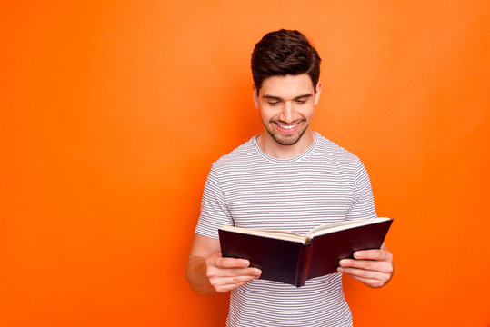 Photo of funny attractive guy hold favorite book hands enjoy reading exciting final intrigue wear striped t-shirt isolated bright orange color background