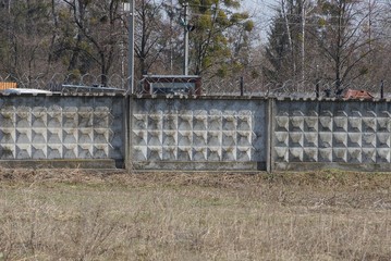 long gray concrete wall of a fence with barbed wire outside in dry grass