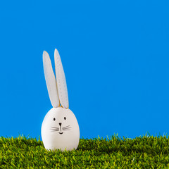 Happy Easter bunny with long ears on green grass and blue background with copy space.