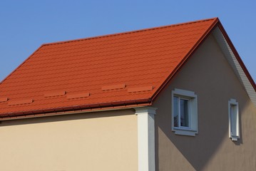large private brown house with white windows under a red tiled roof against a blue sky on a sunny day
