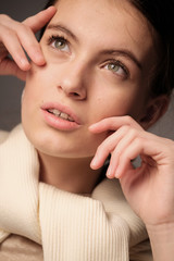 A close-up portrait of a beautiful young girl with brown hair and green eyes with natural makeup in light clothing