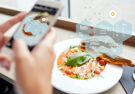 food, eating, technology, culinary and people concept - woman hands with gazpacho soup photo on smartphone screen and nutritional value chart at restaurant