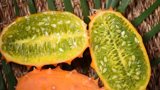 Cuted african horned melon on rotating background. Top view. Exotic Kiwano melon fruits, tropical palm branch. Vegan and raw food concept.