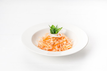 Salad in a white plate with salted cabbage, cucumber, fresh herbs.
