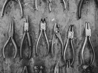 Mechanics tools for repairing an fixing organized on wooden panel board consisted of different sets of pliers in a workshop in black and white