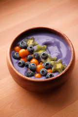 Smoothies of violet color from banana and currant, on top of a blackberry, physalis and kiwi berry. Smoothies in a wooden bowl.