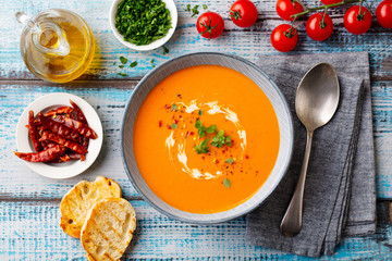Pumpkin cream soup with fresh herbs in a bowl. Blue wooden background. Top view.
