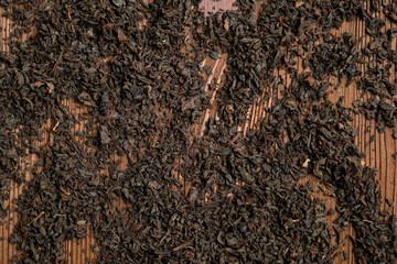 Scattered black tea on a brown wooden background. Top view.