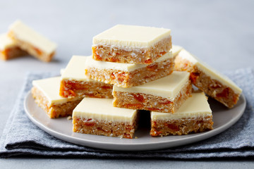 Oat, coconut, apricot bars with white chocolate on a plate. Grey background. Close up.