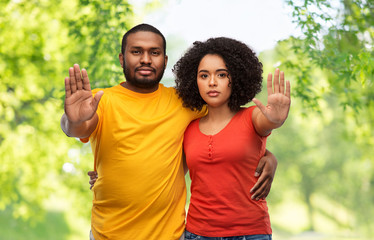 relationships and people concept - african american couple hugging and showing stop gesture over green natural background